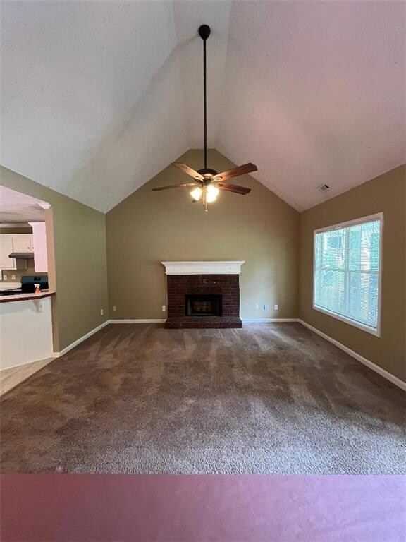 Unfurnished living room featuring dark carpet, ceiling fan, lofted ceiling, a brick fireplace, and baseboards