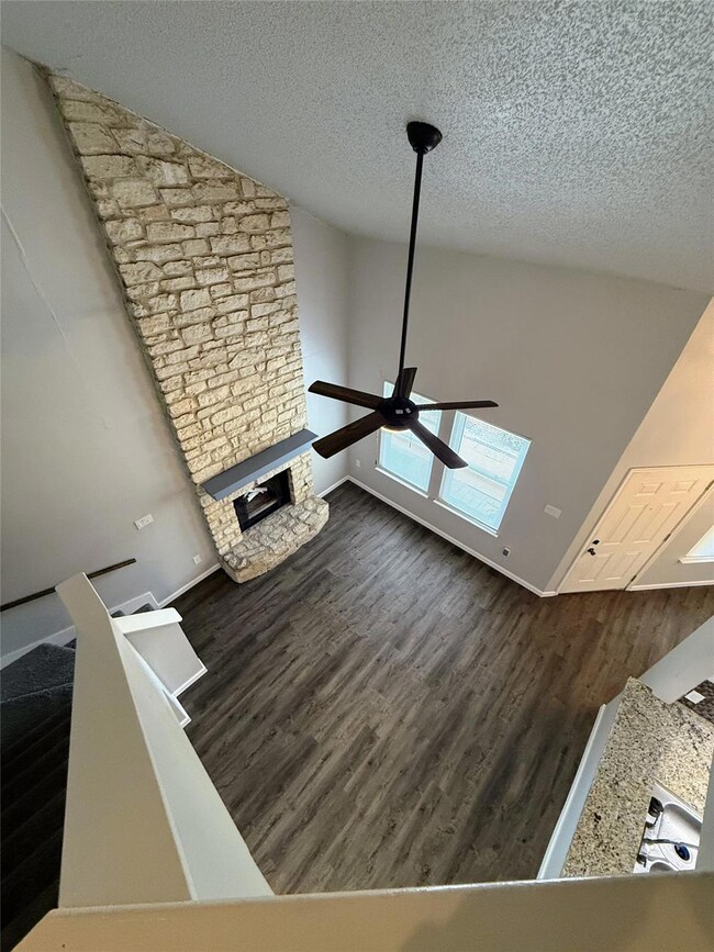 Detailed view of wood finished floors, a stone fireplace, a textured ceiling, and a ceiling fan