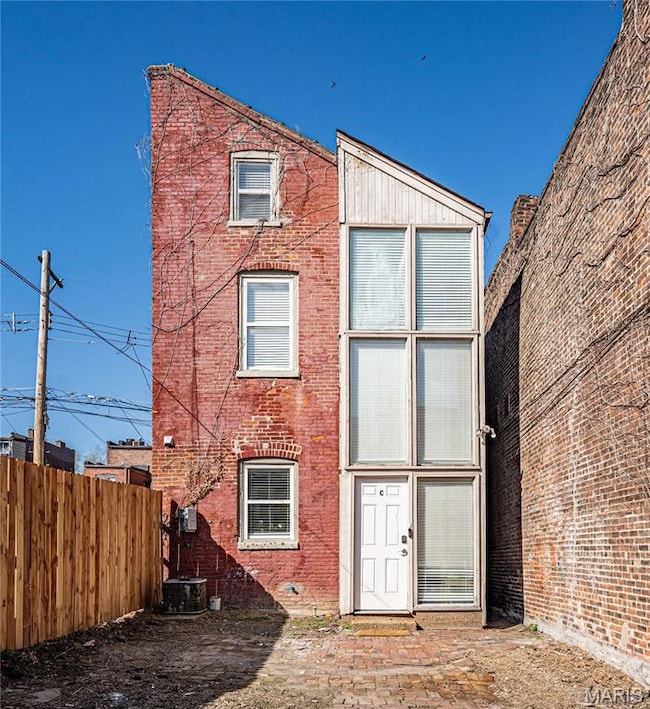 Back of property with fence, brick siding, and central AC