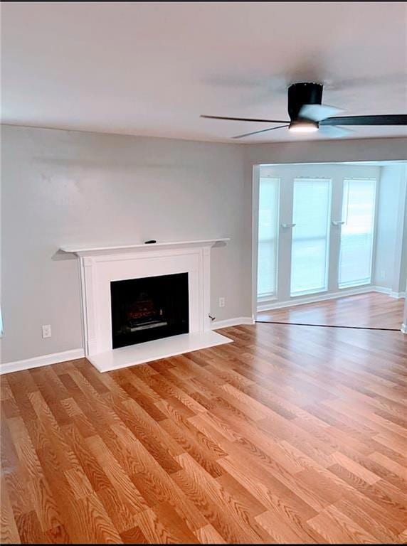 Unfurnished living room featuring a ceiling fan, light wood finished floors, and a fireplace