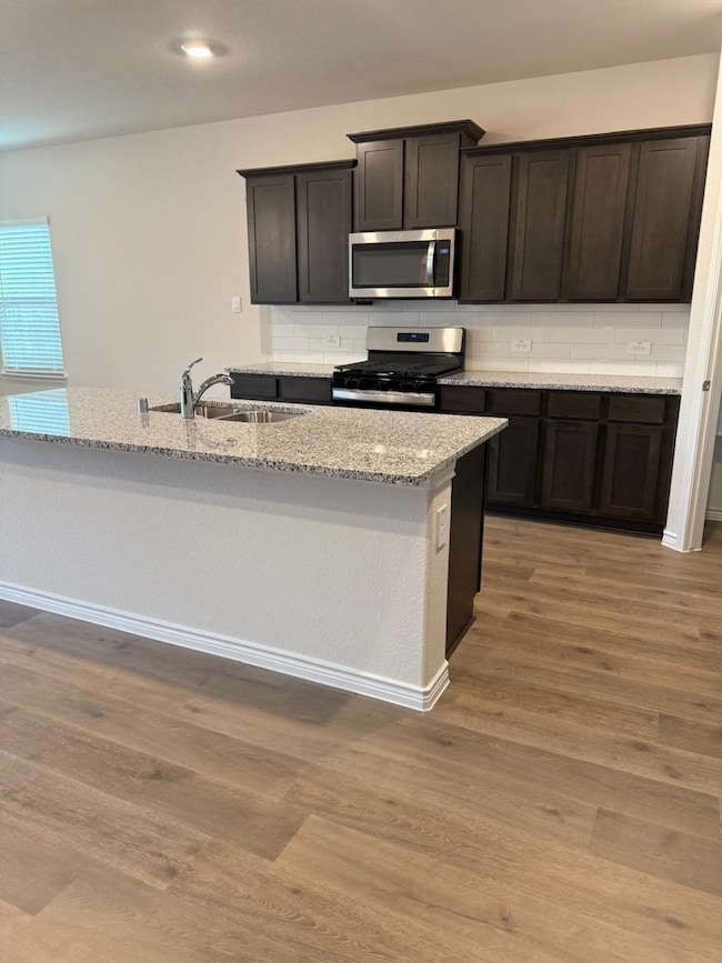 Kitchen featuring tasteful backsplash, stainless steel appliances, light stone counters, light wood-type flooring, and recessed lighting