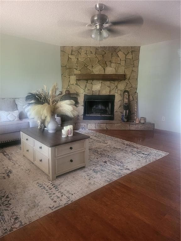 Living area featuring ceiling fan, a stone fireplace, wood finished floors, and a textured ceiling