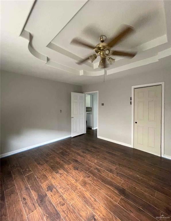 Empty room featuring a raised ceiling, dark wood-type flooring, a ceiling fan, and baseboards