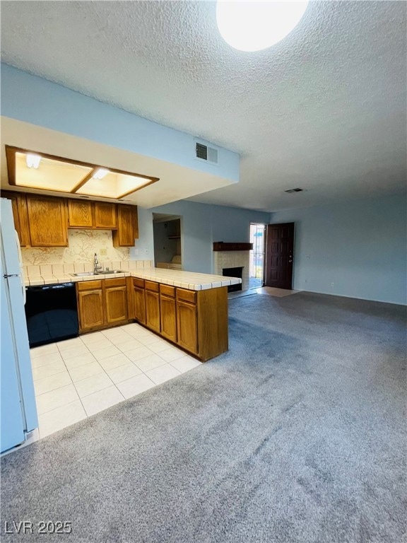 Kitchen featuring brown cabinets, light tile patterned flooring, light colored carpet, a peninsula, and a fireplace