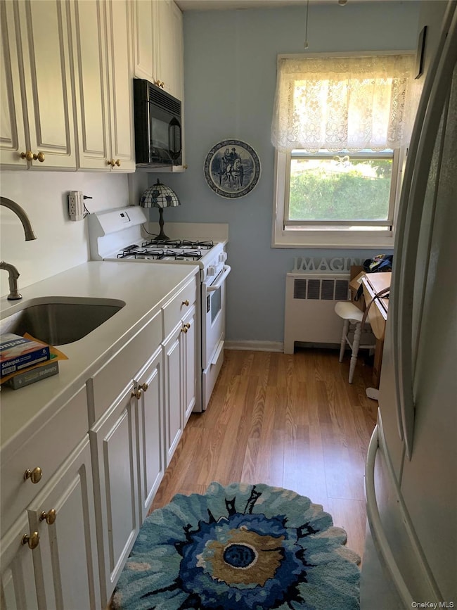 Kitchen featuring gas range gas stove, light wood-style flooring, radiator, black microwave, and freestanding refrigerator