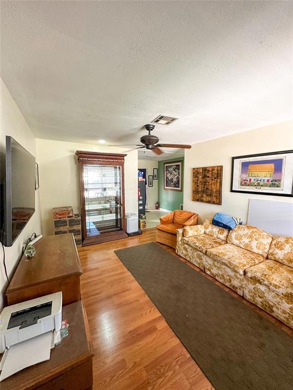 Living area with a textured ceiling, light wood finished floors, and a ceiling fan
