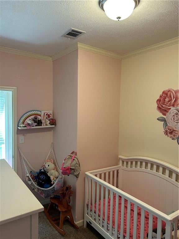 Bedroom with crown molding, a textured ceiling, carpet, and a crib