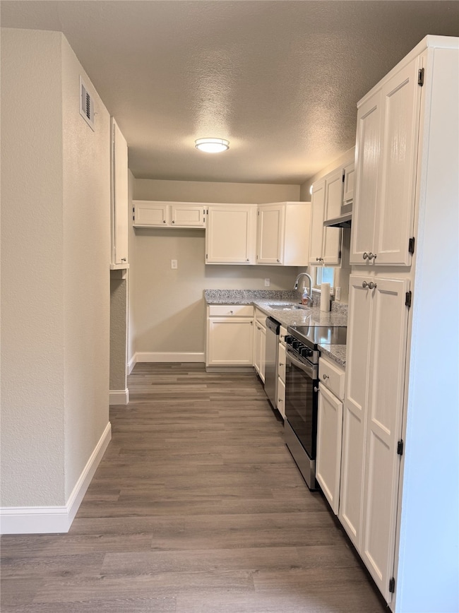 Kitchen featuring appliances with stainless steel finishes, white cabinetry, a textured ceiling, a textured wall, and dark wood-type flooring