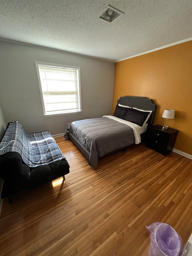 Bedroom with a textured ceiling, wood finished floors, and ornamental molding