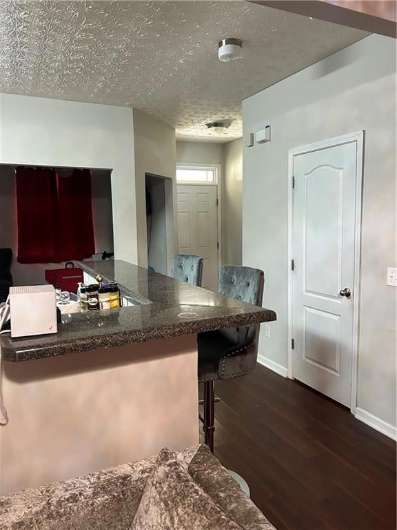 Kitchen with dark wood-style floors, a textured ceiling, and a kitchen bar