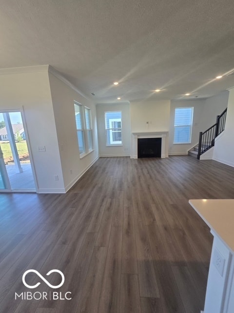 unfurnished living room featuring a textured ceiling, stairs, dark wood-style floors, a fireplace, and plenty of natural light
