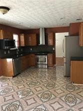 Kitchen with dark countertops, appliances with stainless steel finishes, range hood, and brown cabinetry