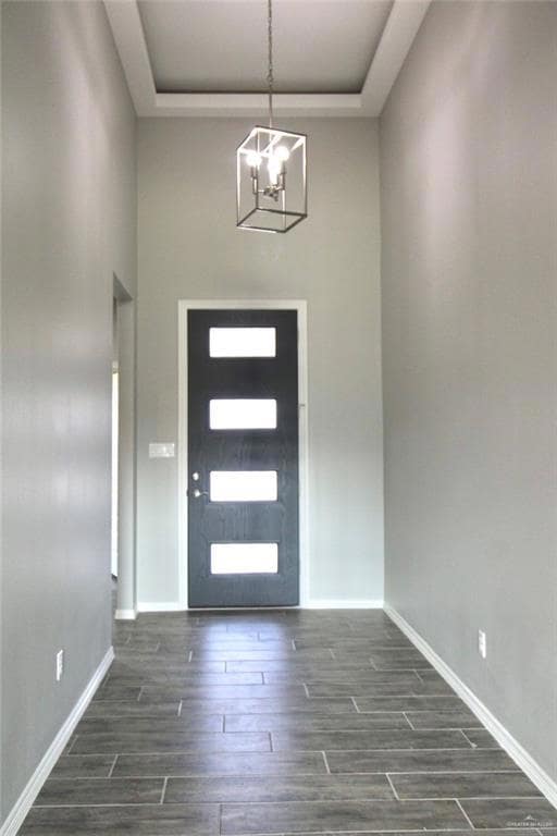 Entryway with a chandelier, a raised ceiling, dark wood-style flooring, and baseboards