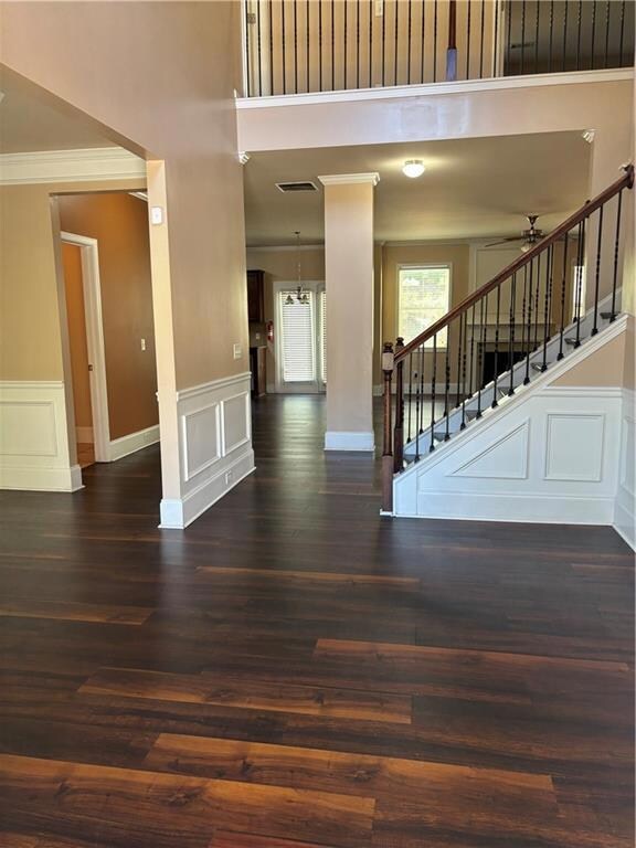 Foyer entrance featuring ornamental molding, a decorative wall, a wainscoted wall, dark wood-type flooring, and stairway