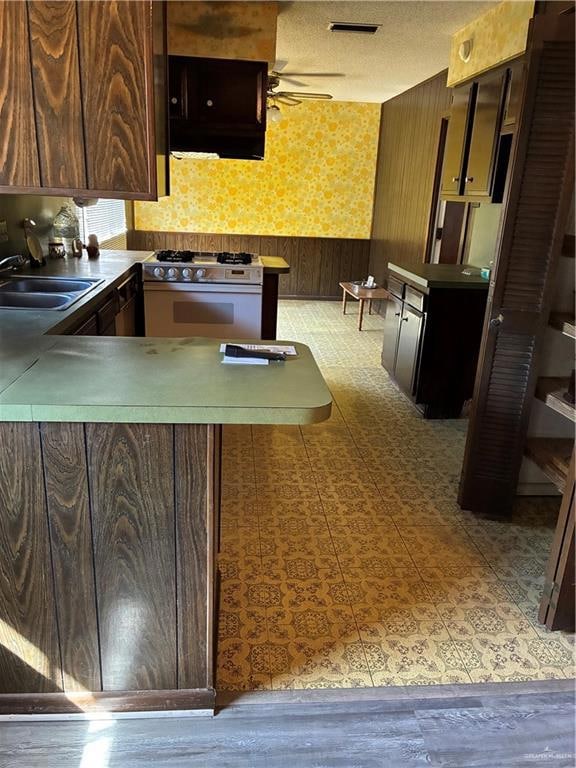Kitchen featuring wallpapered walls, stainless steel range, wood walls, wainscoting, and a textured ceiling