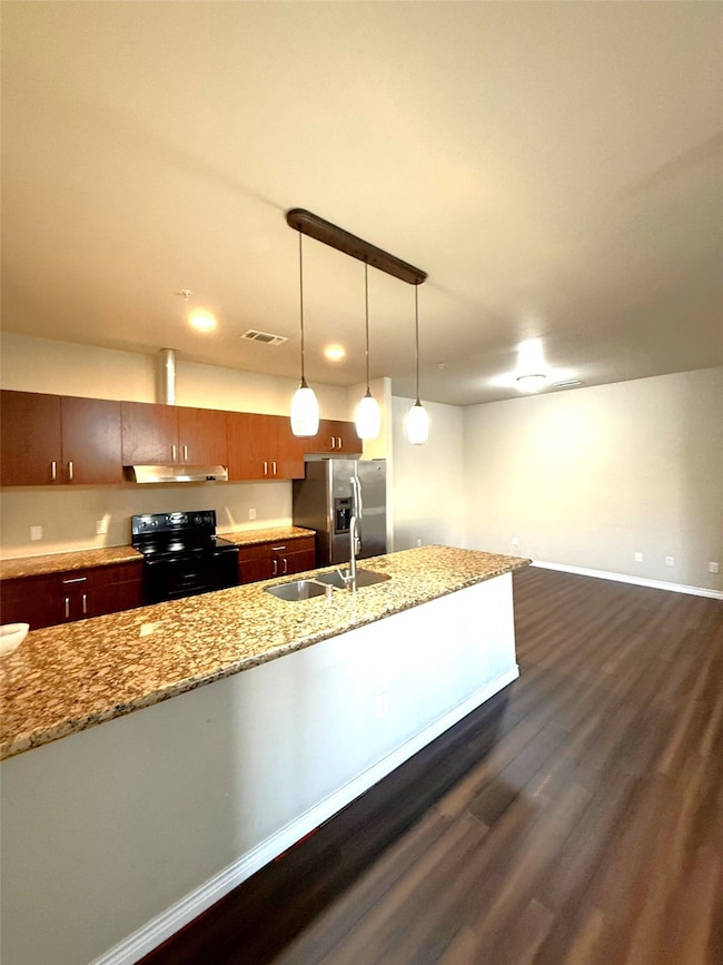 Kitchen with black range with electric stovetop, stainless steel fridge, dark wood finished floors, pendant lighting, and light stone countertops