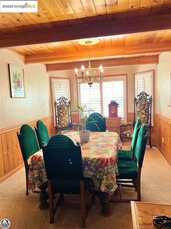 Carpeted dining space featuring beamed ceiling, wooden ceiling, and a chandelier