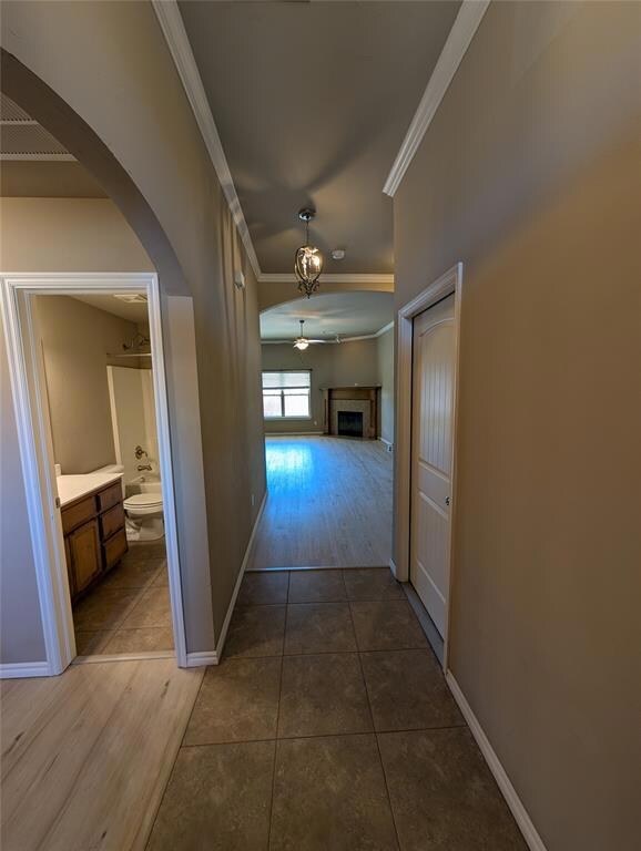 Hallway with visible vents, arched walkways, baseboards, ornamental molding, and tile patterned flooring