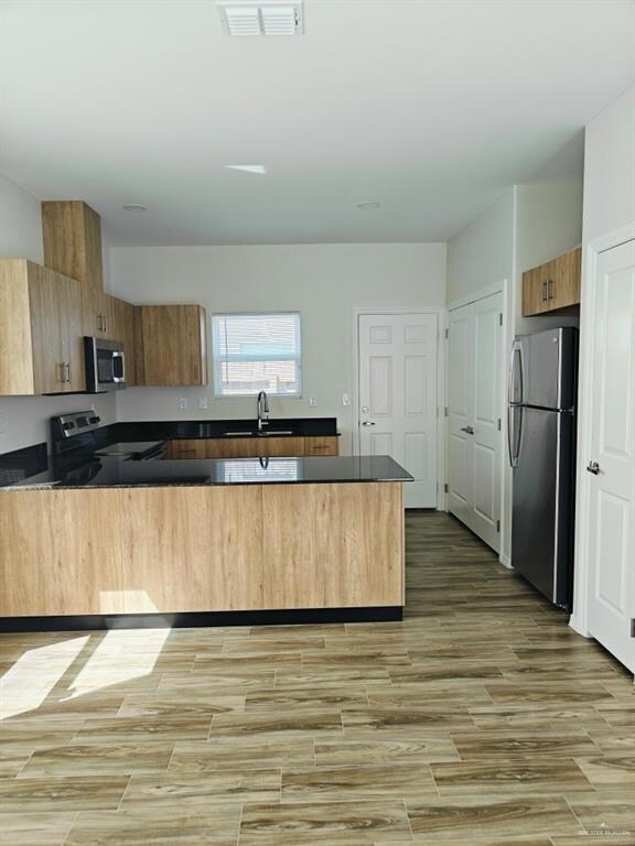 Kitchen featuring a peninsula, visible vents, appliances with stainless steel finishes, a sink, and dark countertops