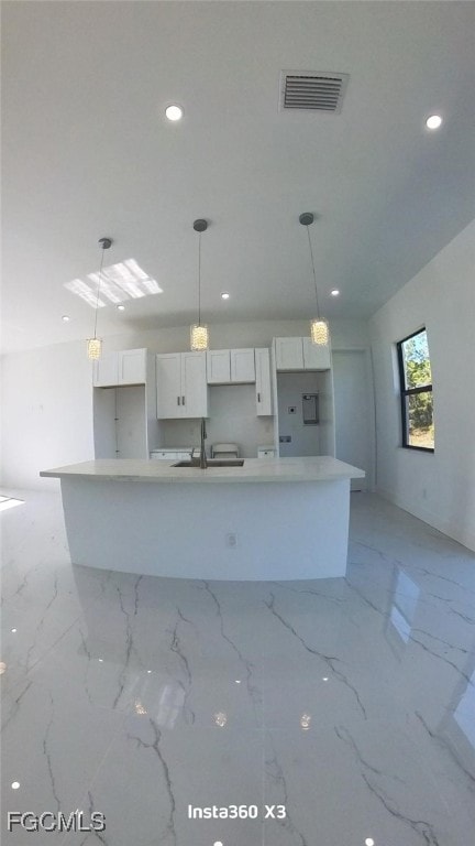 Kitchen with white cabinetry, decorative light fixtures, light stone counters, a center island with sink, and recessed lighting