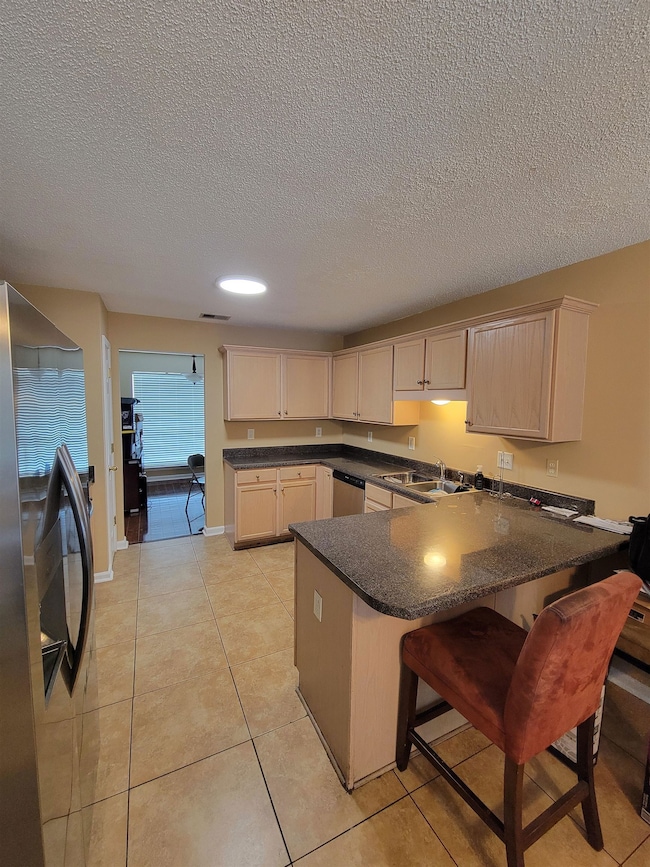 Kitchen featuring appliances with stainless steel finishes, a peninsula, a textured ceiling, a kitchen bar, and light tile patterned floors