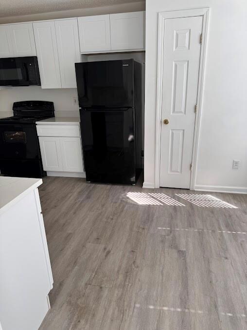 Kitchen featuring black appliances, light wood finished floors, white cabinets, and baseboards