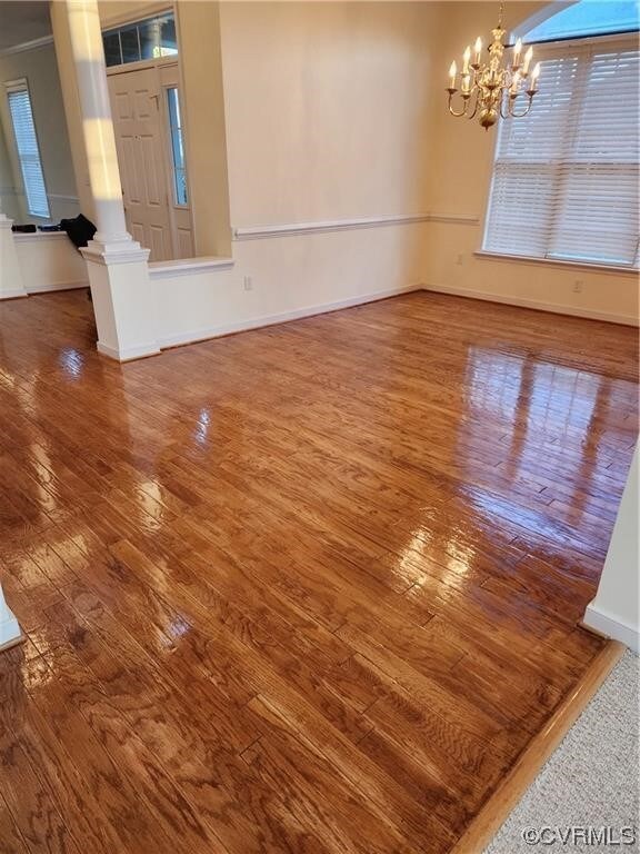 Empty room with dark hardwood / wood-style floors, ornamental molding, ornate columns, and an inviting chandelier