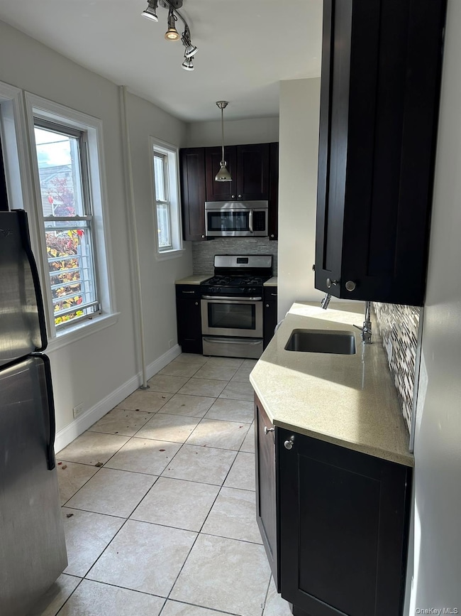 Kitchen featuring decorative backsplash, stainless steel appliances, dark cabinets, light tile patterned floors, and decorative light fixtures