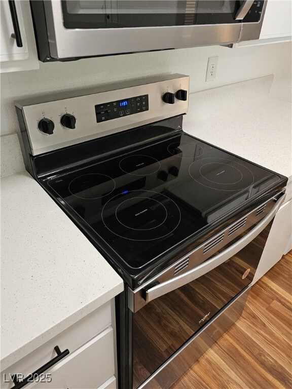 Kitchen view of stainless steel appliances, light stone counters, wood finished floors, and white cabinetry