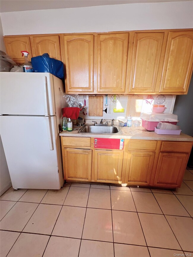 Kitchen with freestanding refrigerator, light countertops, light tile patterned floors, and light brown cabinets