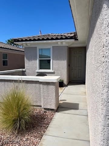 View of exterior entry with stucco siding and a tiled roof