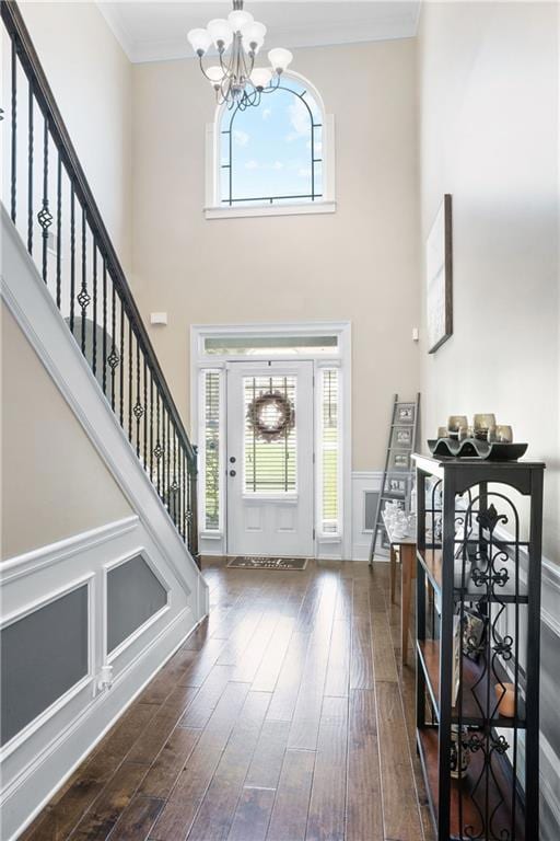 Foyer entrance with a chandelier, wood finished floors, ornamental molding, stairway, and a high ceiling