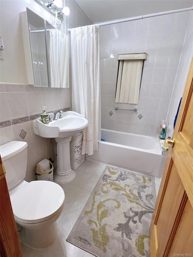 Bathroom with tile walls, shower / bath combination with curtain, and light tile patterned floors
