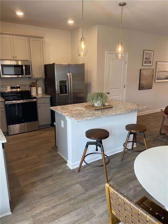 Kitchen featuring a breakfast bar, appliances with stainless steel finishes, light stone counters, hanging light fixtures, and dark wood-style flooring