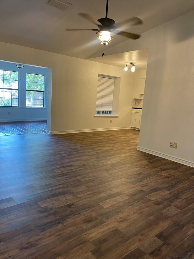 Unfurnished living room featuring dark wood-style floors, a ceiling fan, and vaulted ceiling