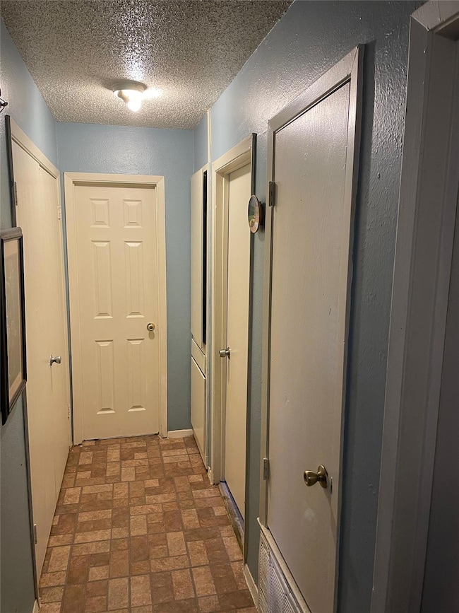 Hall featuring brick patterned floor, a textured 