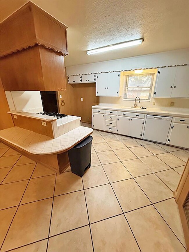 Kitchen featuring sink, white appliances, white cabinets, a textured ceiling, and tile countertops
