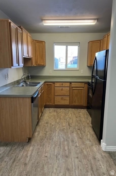 Kitchen featuring black appliances, light wood-style floors, brown cabinetry, and dark countertops