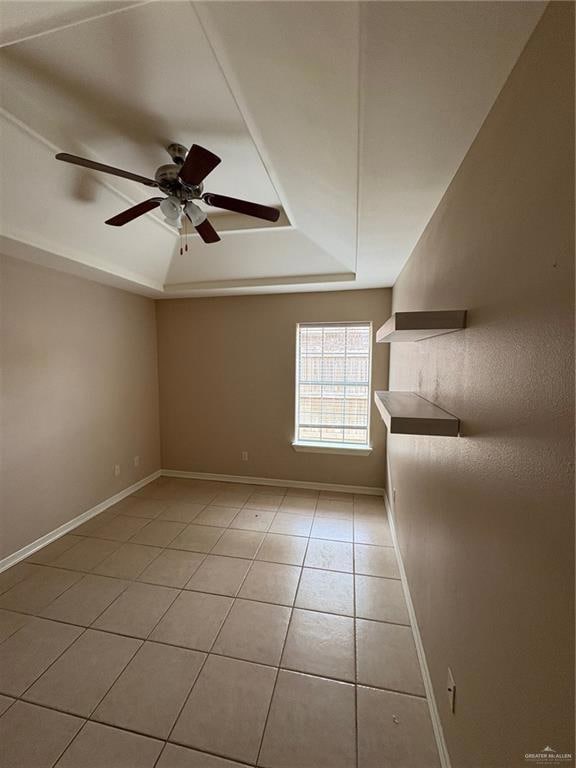 Empty room with a tray ceiling, light tile patterned floors, a ceiling fan, and baseboards