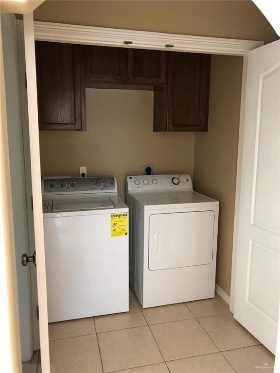 Clothes washing area with cabinet space, washing machine and dryer, and light tile patterned floors