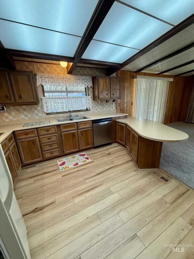 Kitchen featuring dishwasher, a peninsula, light countertops, light wood-style flooring, and beam ceiling