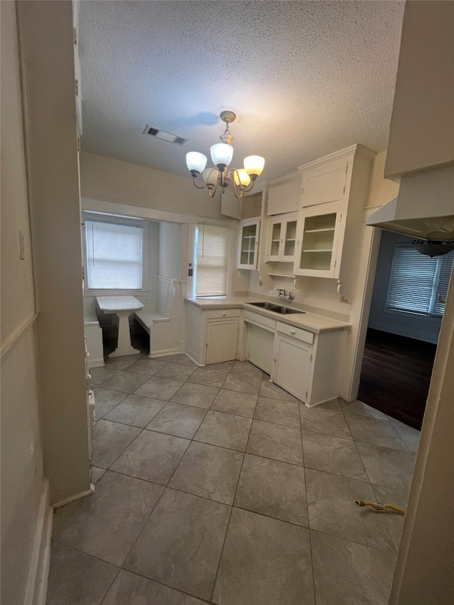 Kitchen featuring a textured ceiling, light countertops, white cabinetry, a chandelier, and glass insert cabinets