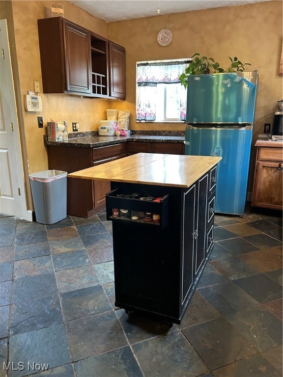 Kitchen featuring fridge, open shelves, a center island, butcher block counters, and stone tile flooring