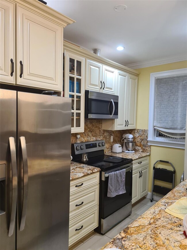 Kitchen featuring appliances with stainless steel finishes, cream cabinetry, ornamental molding, decorative backsplash, and recessed lighting