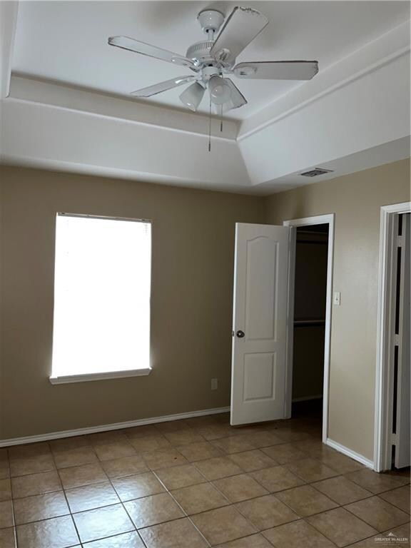Unfurnished room featuring baseboards, visible vents, ceiling fan, and a raised ceiling