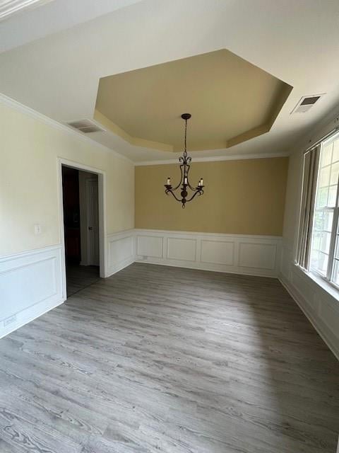 Unfurnished dining area with a tray ceiling, a chandelier, crown molding, wood finished floors, and a decorative wall