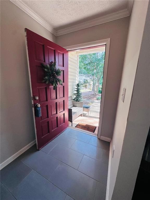 Foyer entrance with ornamental molding, baseboards, dark tile patterned flooring, and a textured ceiling