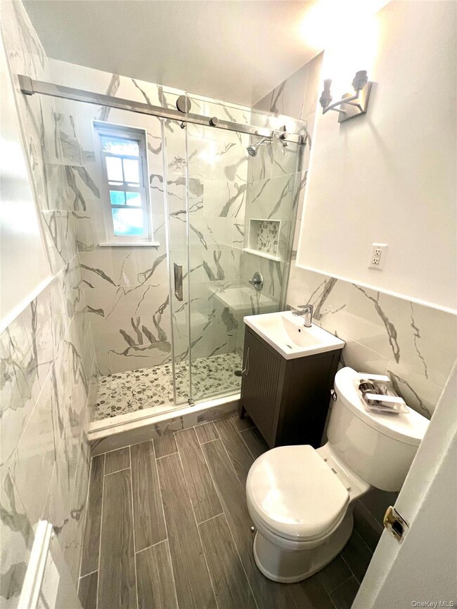Bathroom with tile walls, a marble finish shower, vanity, wainscoting, and wood finish floors