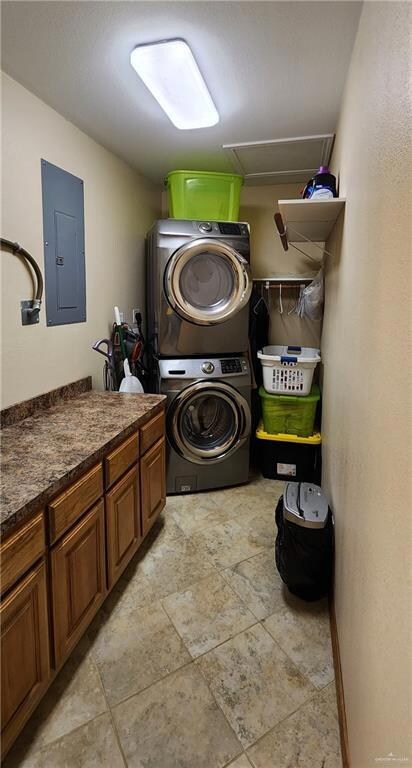 Clothes washing area featuring light tile floors, cabinets, and stacked washing maching and dryer