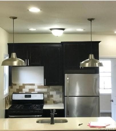 Kitchen with decorative light fixtures, appliances with stainless steel finishes, dark cabinets, decorative backsplash, and recessed lighting